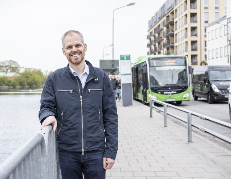 Fredrik Holmlund på Trafikverket står utomhus på en bro och håller i räcket. Han ler mot kamera. Bakom honom syns en grön buss från Skånetrafiken.
