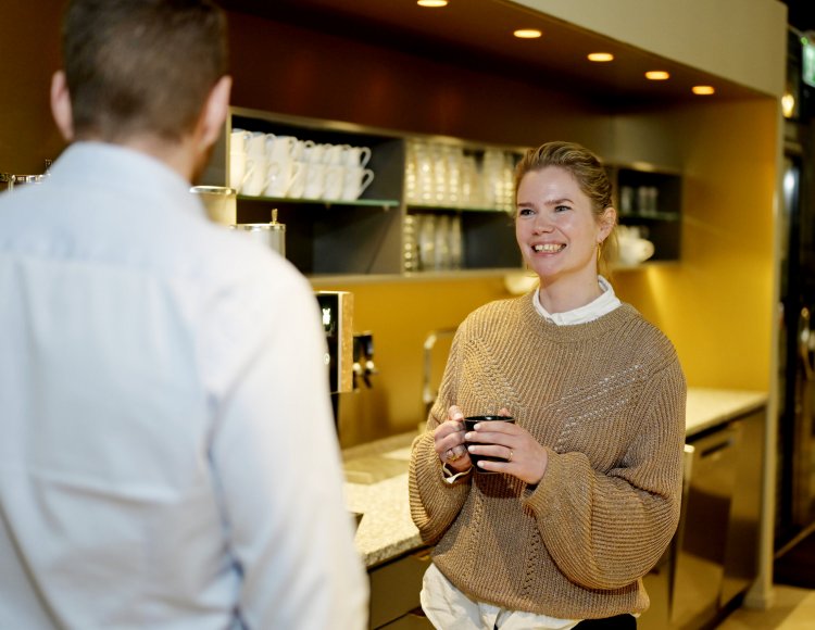 Helene Andersson ler mot en kollega i ett kontorskök.