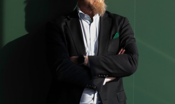 Thomas Holmberg står i solljus framför en grön vägg. 