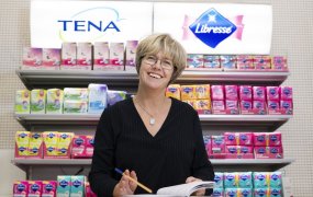 Anna-carin Elfström ståendes framför en hylla full av essitys färgglada produkter som Tena och Libress.