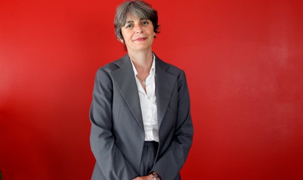 Pascale Gimenez står i grå kostym framför en röd vägg.