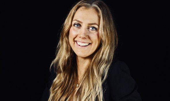Carolin Solskär sitter vid ett bord i en studio med svart bakgrund.