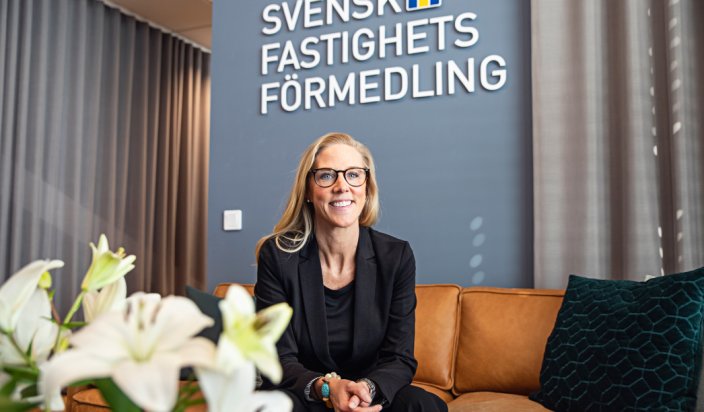 Josefin Thörnert är rekryteringschef på Svensk Fastighetsförmedling. Hon sitter framåtlutad i en congacfärgad skinnsoffa och ler mot kameran. På den blågrå väggen bakom sitter Svensk Fastighetsförmedlings logotyp. I förgrunden syns en bukett vita liljor.