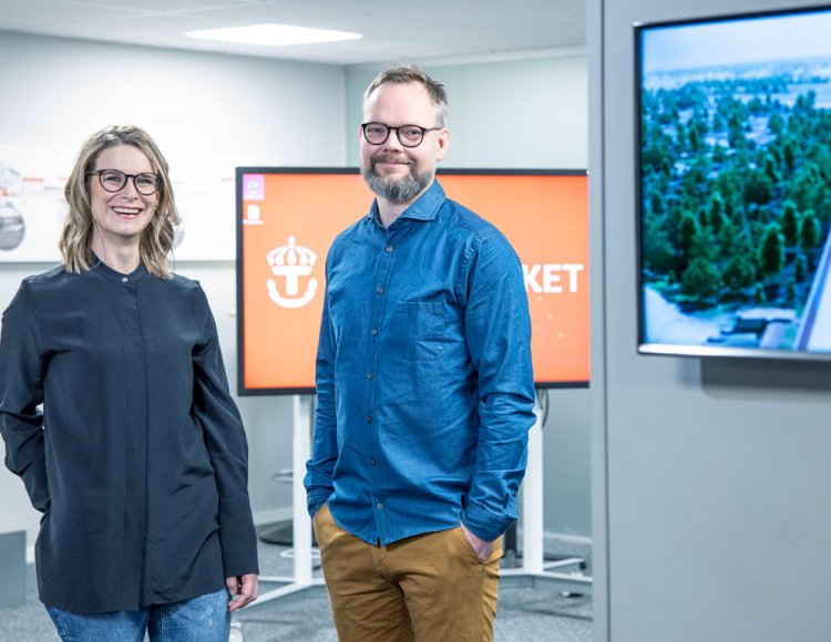 Lena Hägg och Kristofer Södergberg står i en av Trafikverkets lokaler med två stora skärmar i bakgrunden.