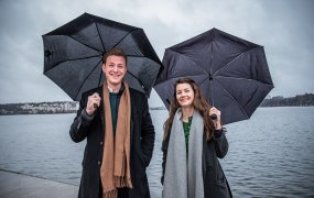 Ida Landin och Jonas Lundgren står utomhus under varsitt paraply med vatten i bakgrunden.