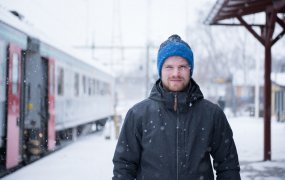 Johannes Nilsson står på en tågstation med varma ytterkläder och snö som faller.