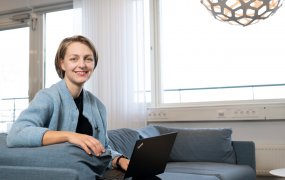 Hanna Ekberg sitter i en soffa med en dator i knät, och ett fönster i bakgrunden.