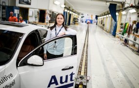 Hanna Karlsson står bredvid en bil med ena armen lutandes mot bildörren, i Autolivs testrum. 