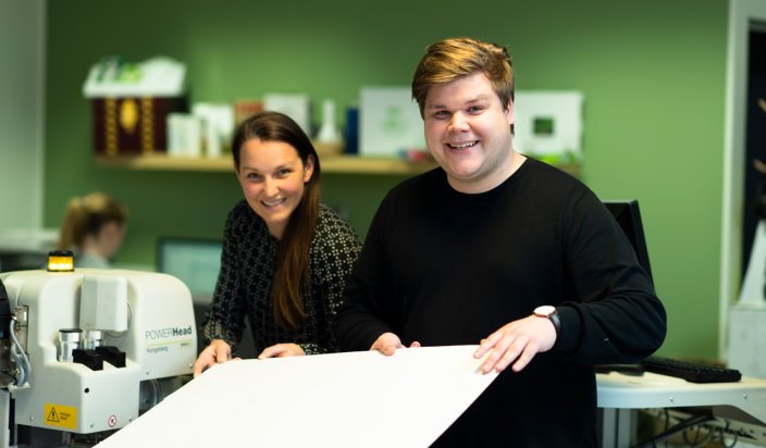 Carl Johansson visar en skogsindustribolagets produkter i form av ett stort vitt ark tillsammans med en kollega. 