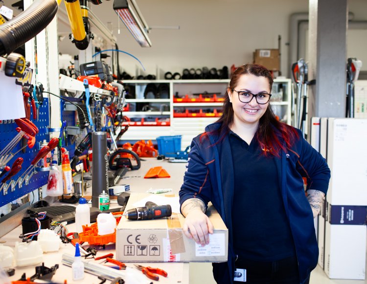 Alba Sadikovska, labbingenjör på Husqvarna Group, står i en garageliknande byggnad, vid en arbetsbänk. På bänken ligger massor av olika verktyg. 