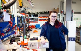 Alba Sadikovska, labbingenjör på Husqvarna Group, står i en garageliknande byggnad, vid en arbetsbänk. På bänken ligger massor av olika verktyg. 