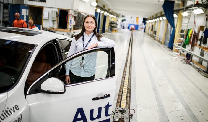 Projektingenjören Hanna ståendes bredvid en testbil i den stora verkstaden. 