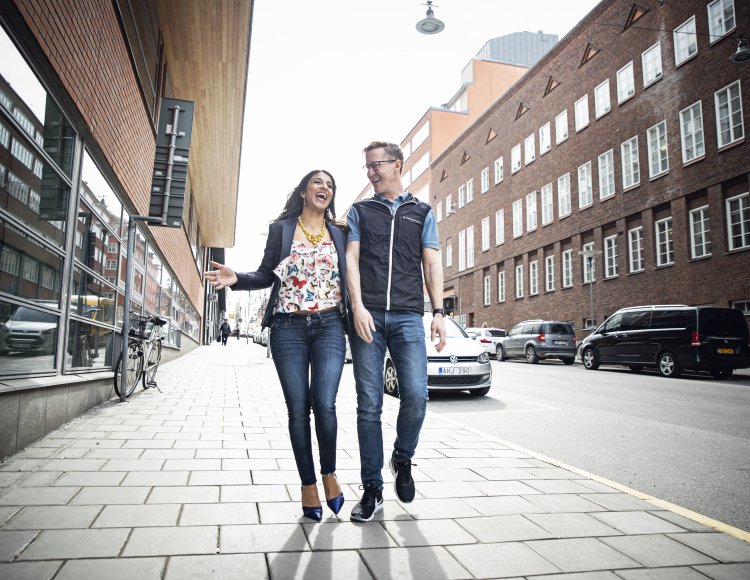 Carolina och Johan går skrattandes på gatan mellan två tegelbyggnader.