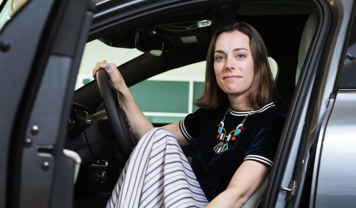 Emelie Emanuelsson, Volvo. Emelie sitter i en bil med förardörren öppen och tittar in i kameran. Ena handen har hon på ratten. 