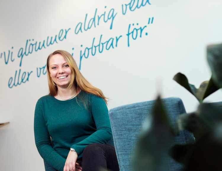 Jessica Hultgren, elektroingenjör på Göteborg Energi, sitter på kontoret och ler mot kameran. I förgrunden syns en turkos stol och en krukväxt, och på väggen bakom henne står det skrivet 